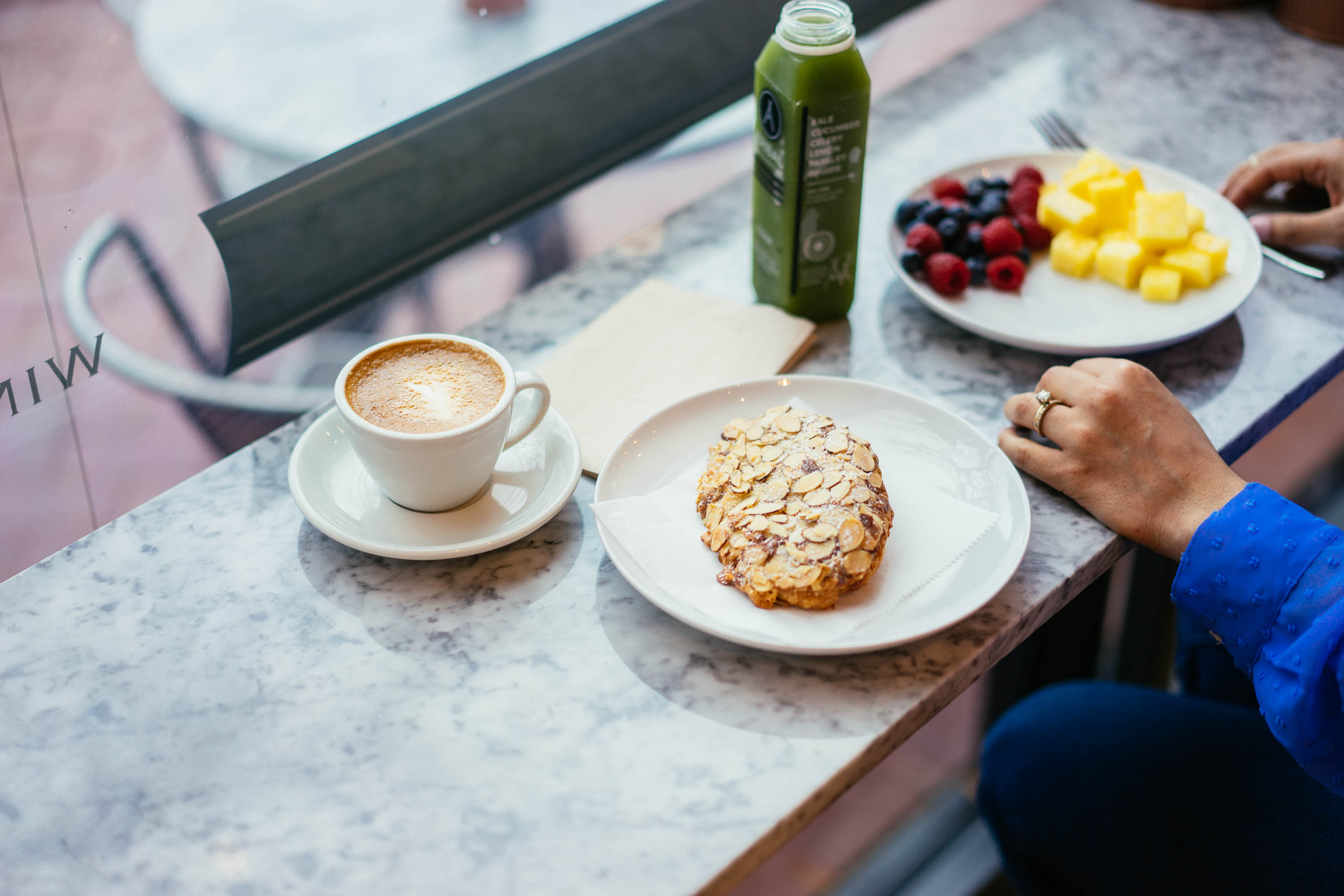 Countertop with coffee, croissant, fruit, and green juice.